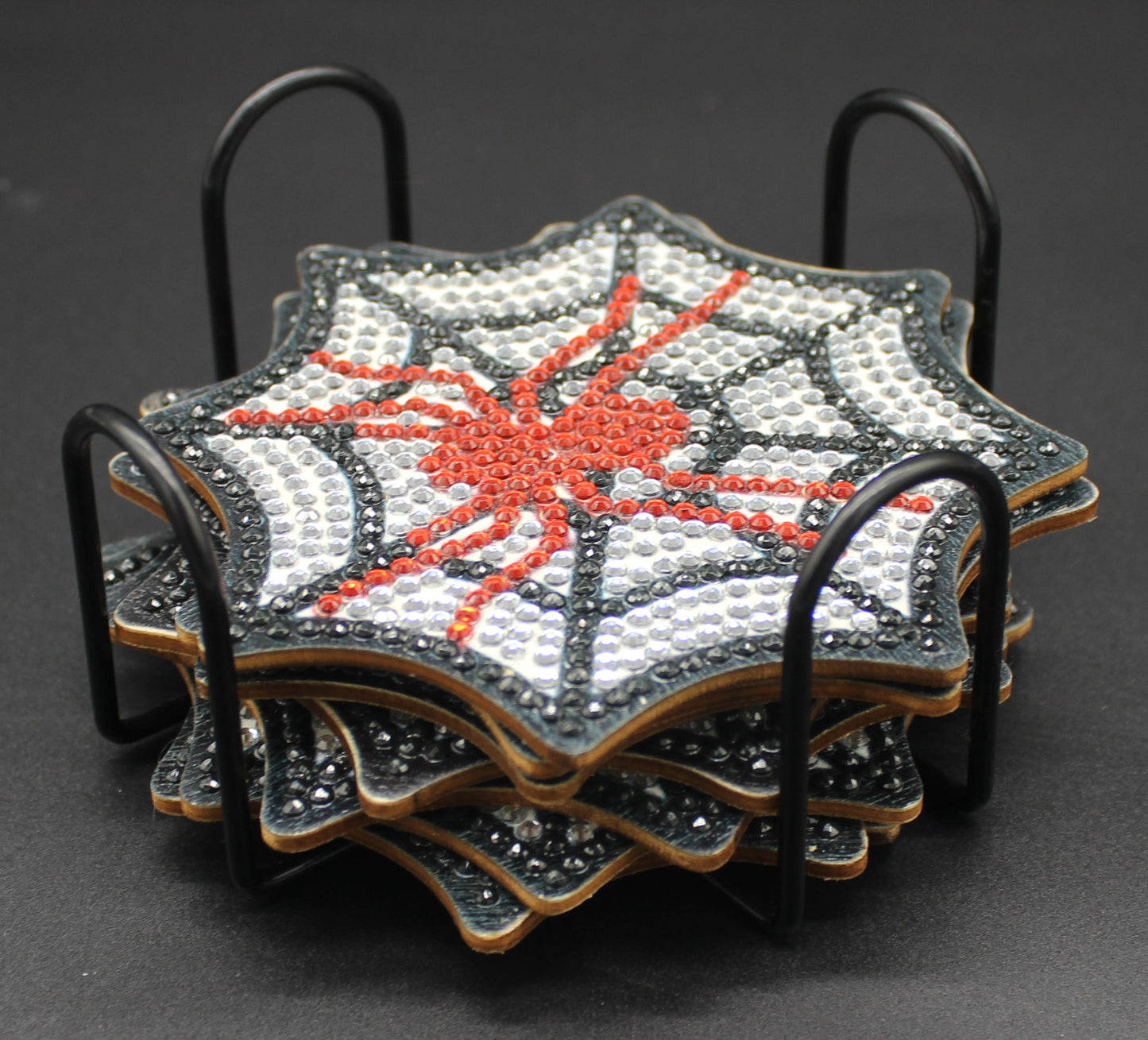 Set of four spiderweb-themed coasters in a metal holder on a dark background
