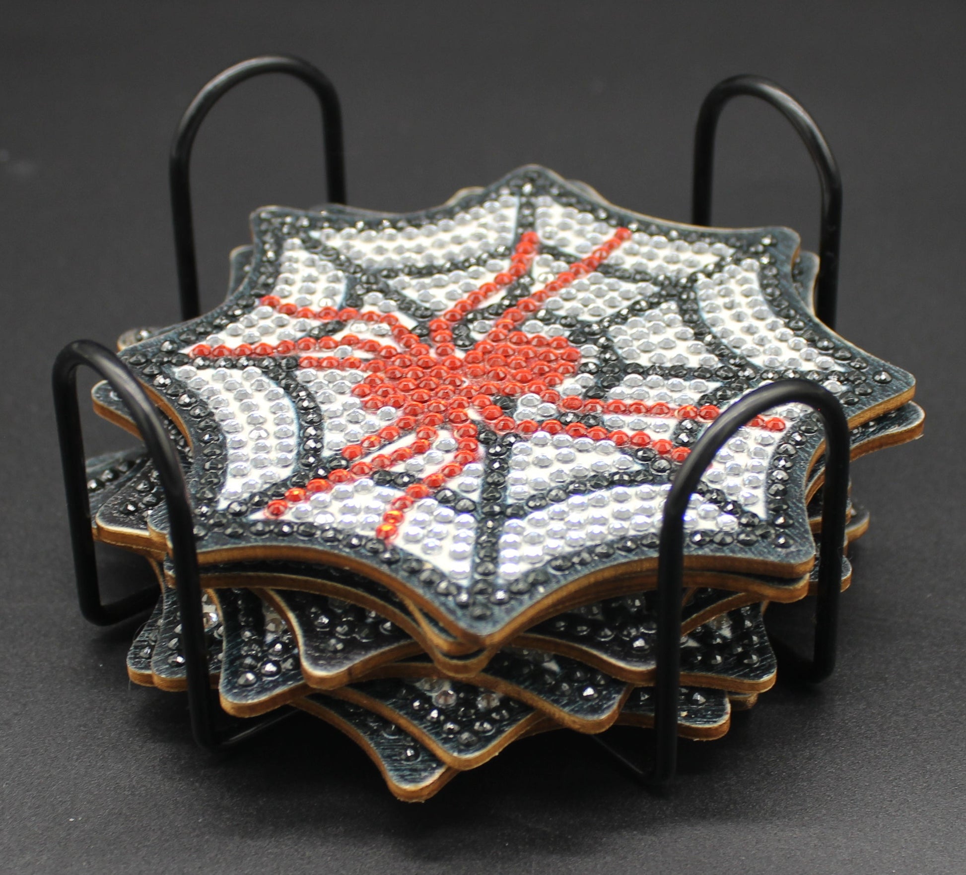Set of four spiderweb-themed coasters in a metal holder on a dark background