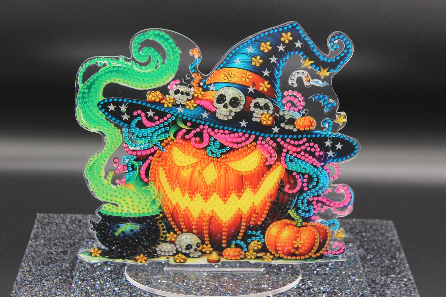 Colorful Halloween-themed decorative piece with a jack-o'-lantern, witch hat, and ghosts on a dark background.