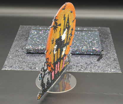 Decorative feather with beadwork on a stand against a dark background