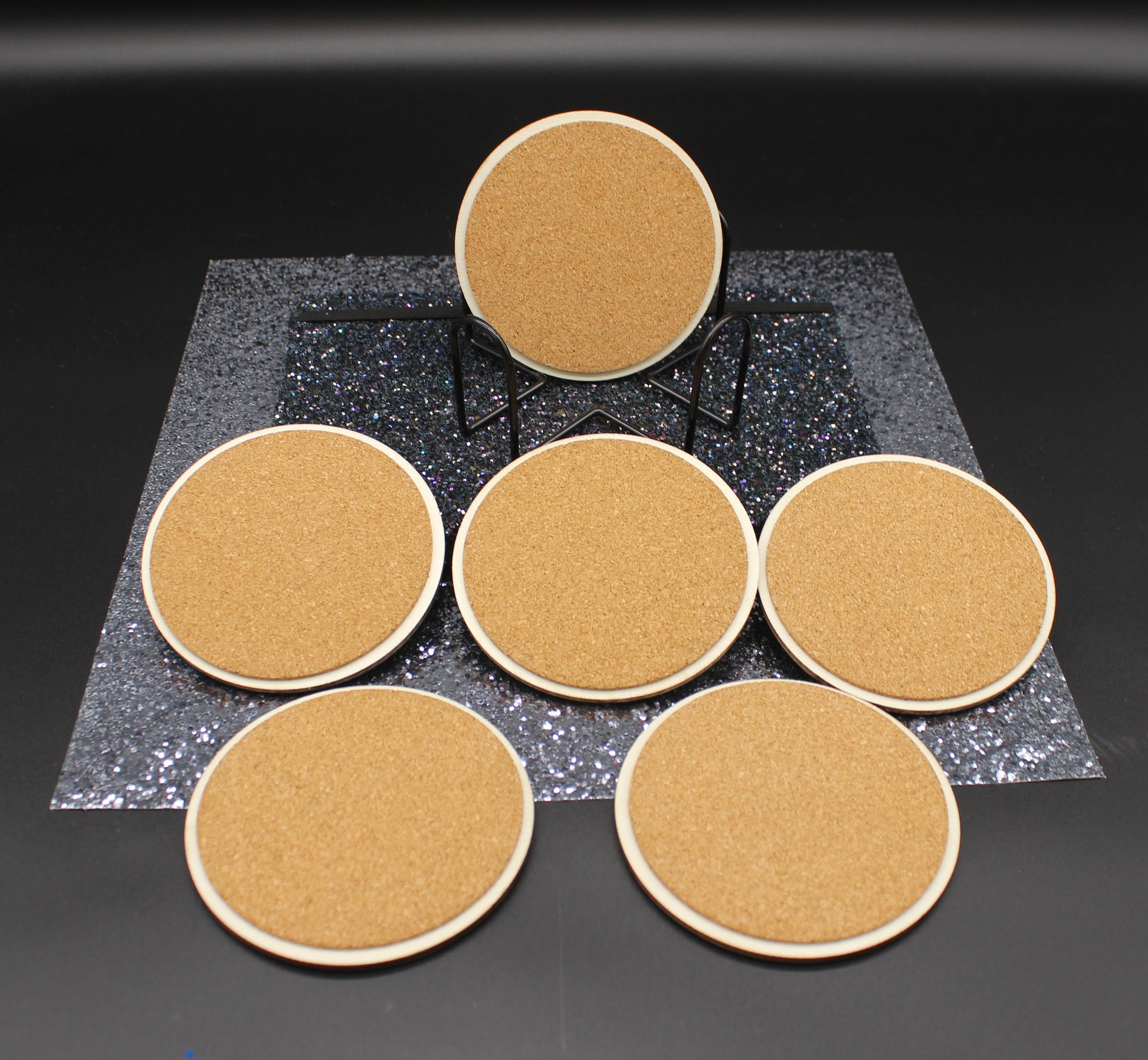 Set of six round cork coasters on a black surface with a dark gray textured square in the center.
