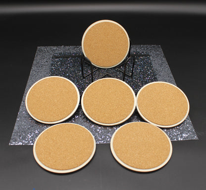Set of six round cork coasters on a black surface with a dark gray textured square in the center.
