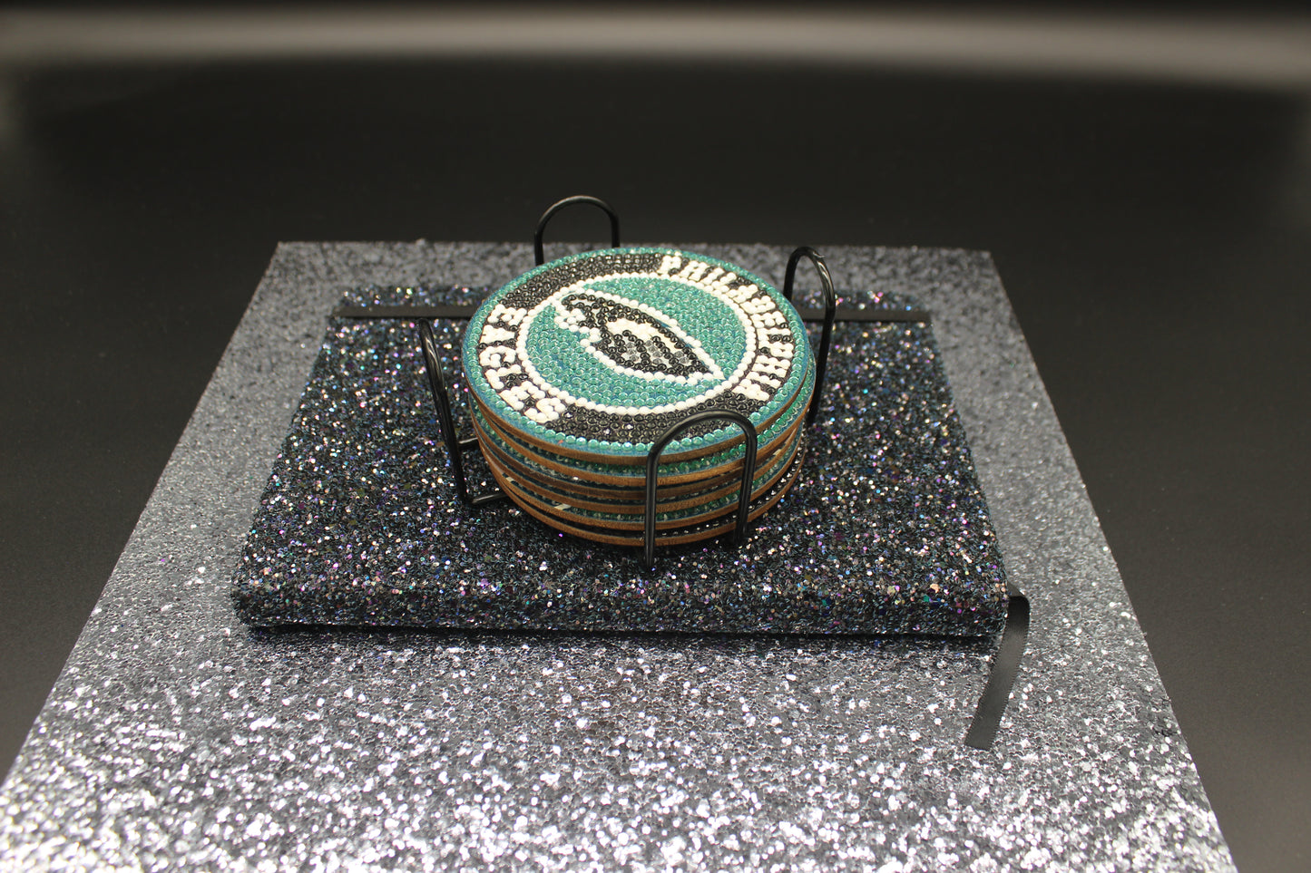 Stack of green coasters with a logo on a black stand against a dark background