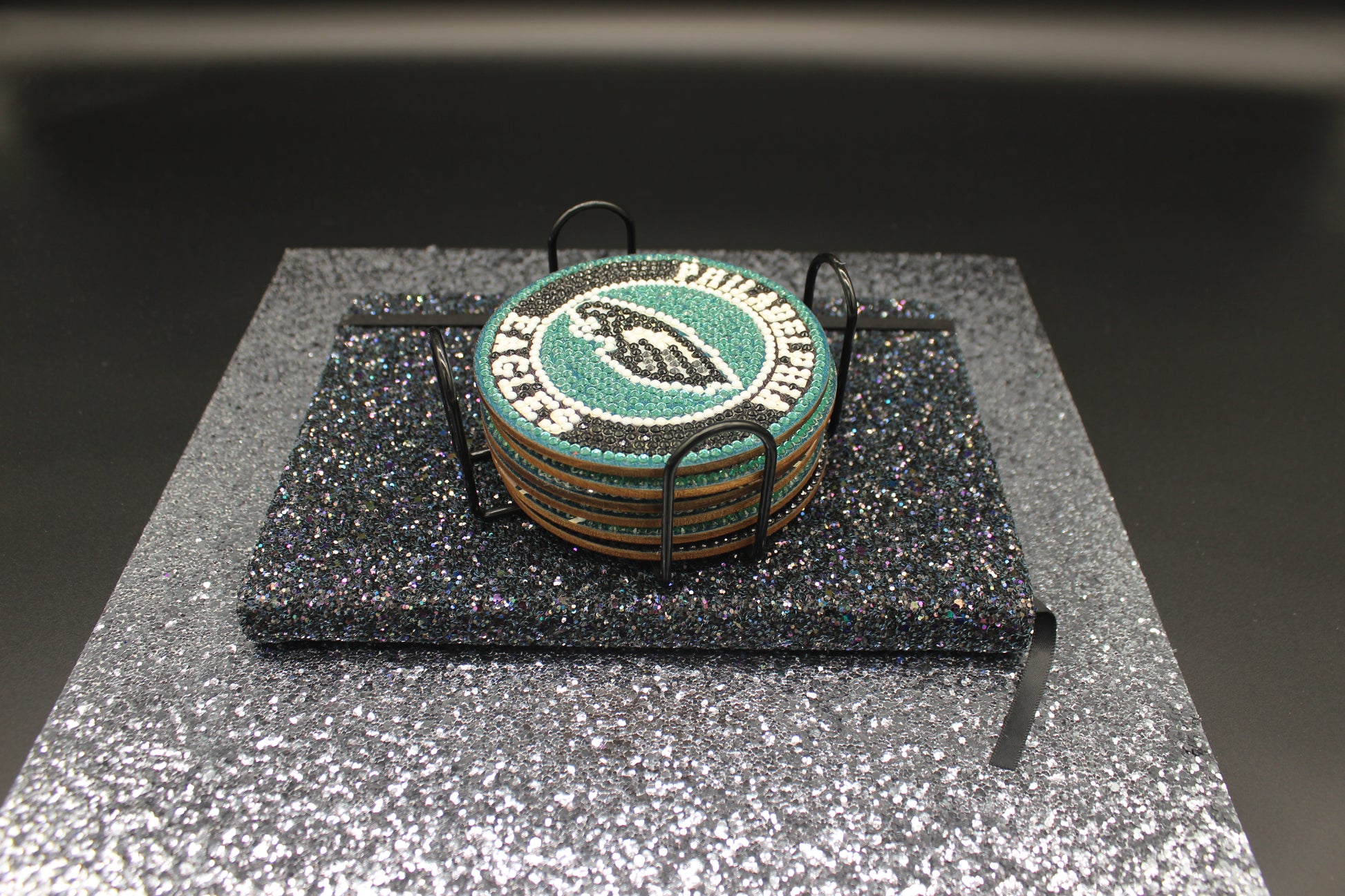 Stack of green coasters with a logo on a black stand against a dark background