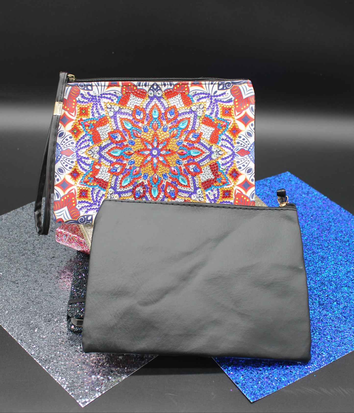 Two pouches, one with a colorful mandala pattern and the other black, on a reflective surface.