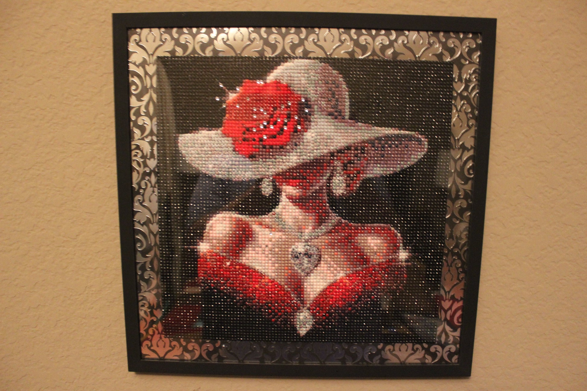 Decorative wall art with a woman wearing a red dress and white hat, framed in black with decorative patterns.