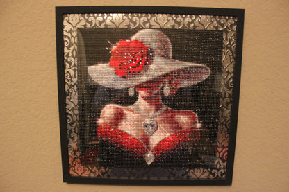 Decorative wall art with a woman wearing a red dress and white hat, framed in black with decorative patterns.