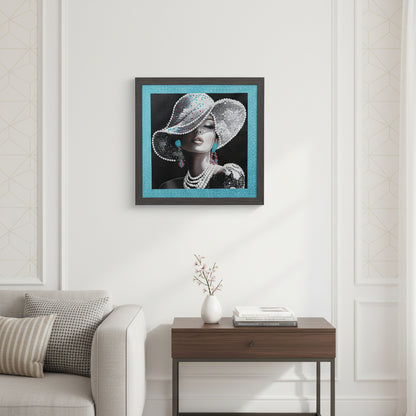 A framed fashion portrait artwork showing a woman in profile wearing an ornate glittery hat, pearl necklace, and dangling earrings, set against a black background with a bright blue glitter border and dark frame.